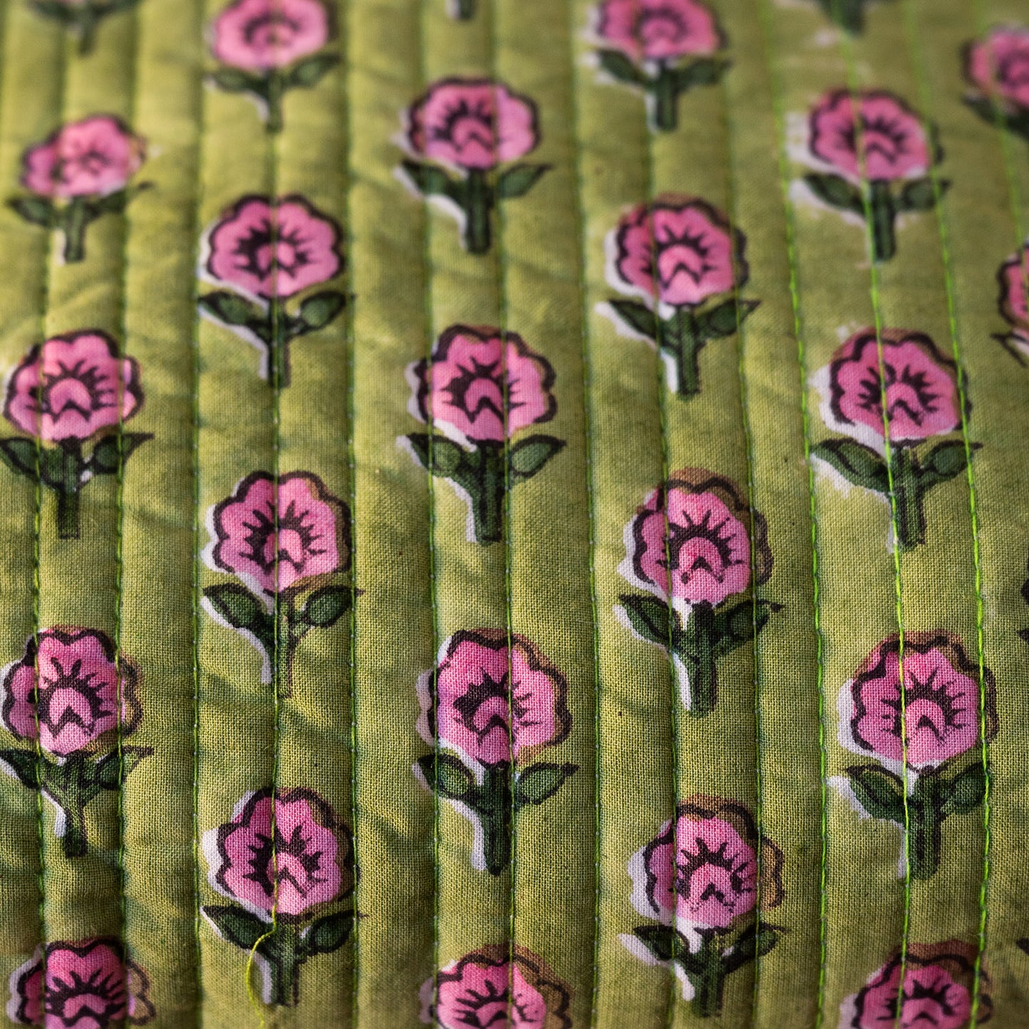 Close-up of a quilted fabric with a repeating floral pattern featuring pink flowers with green stems on an olive green background.