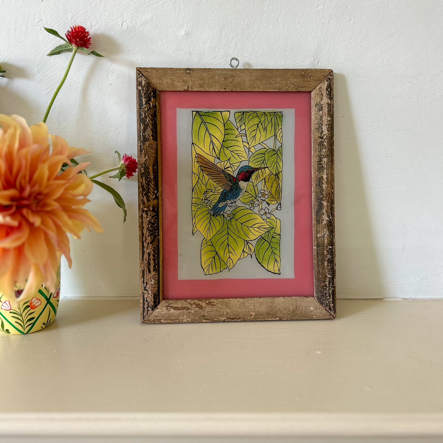 Framed artwork of a hummingbird on a pink background with flowers beside it.onstance-and-denny-indian-reverse-glass-painting-boxed-packaging-hand-painted-artisan-art-HUMMINGBIRD