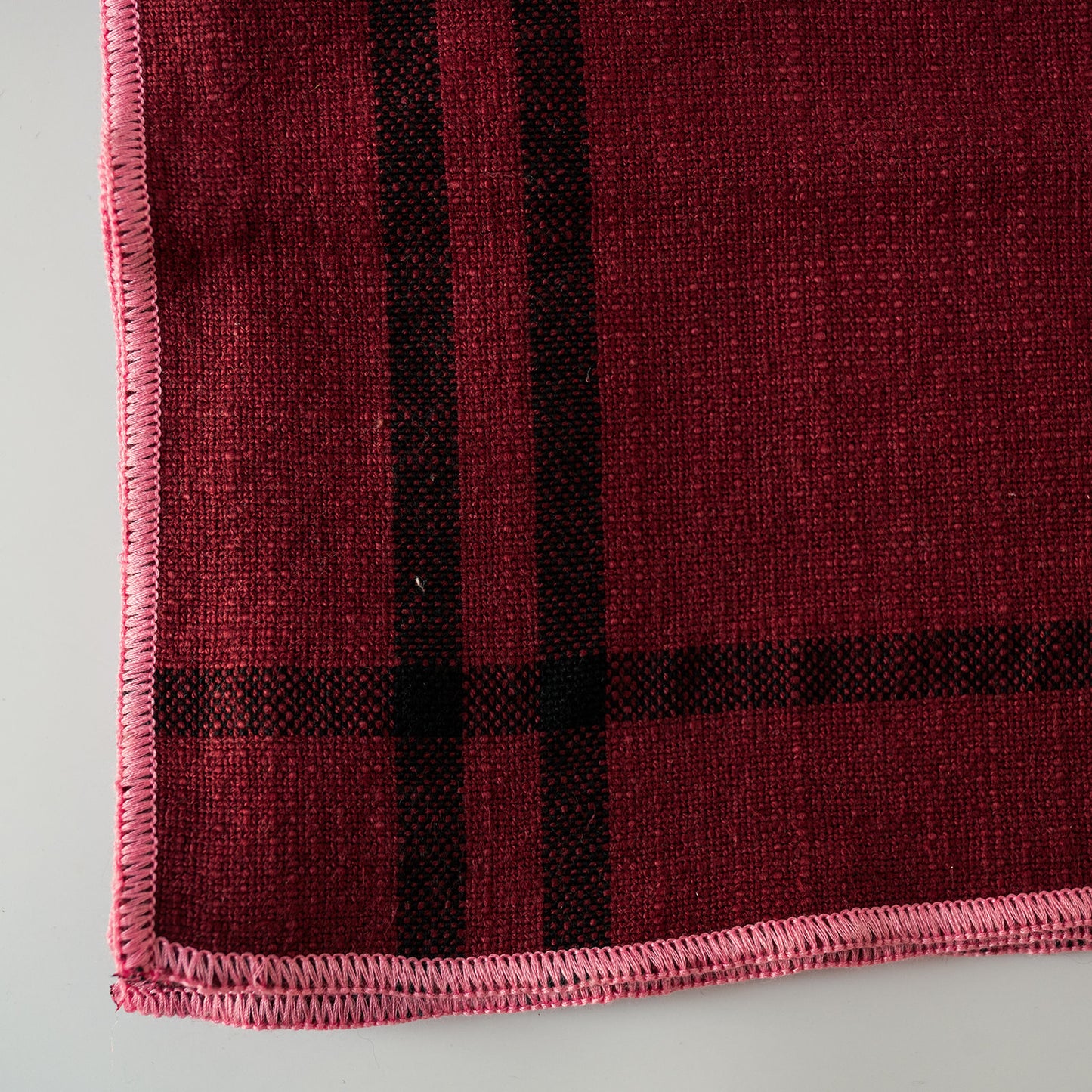 A close-up of a woven textile, likely a blanket, throw, or scarf, featuring a RED and black plaid pattern with a bright blue fringed edge.