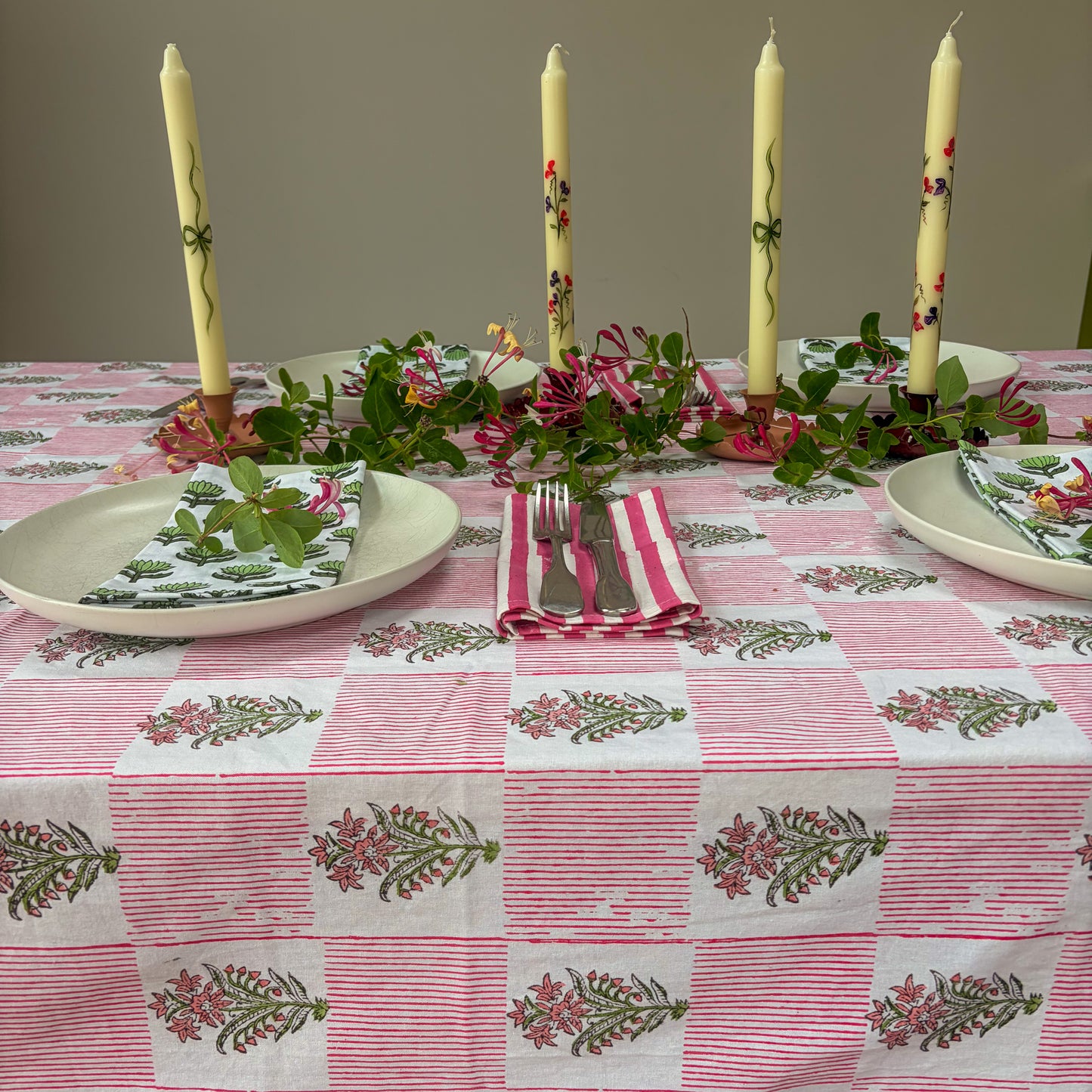 Table setting with floral-patterned tablecloth, plates, napkins, and candles.