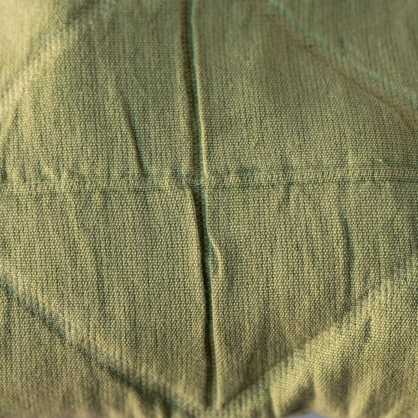 A close-up of olive green quilted fabric with a central vertical seam and stitched panel lines.