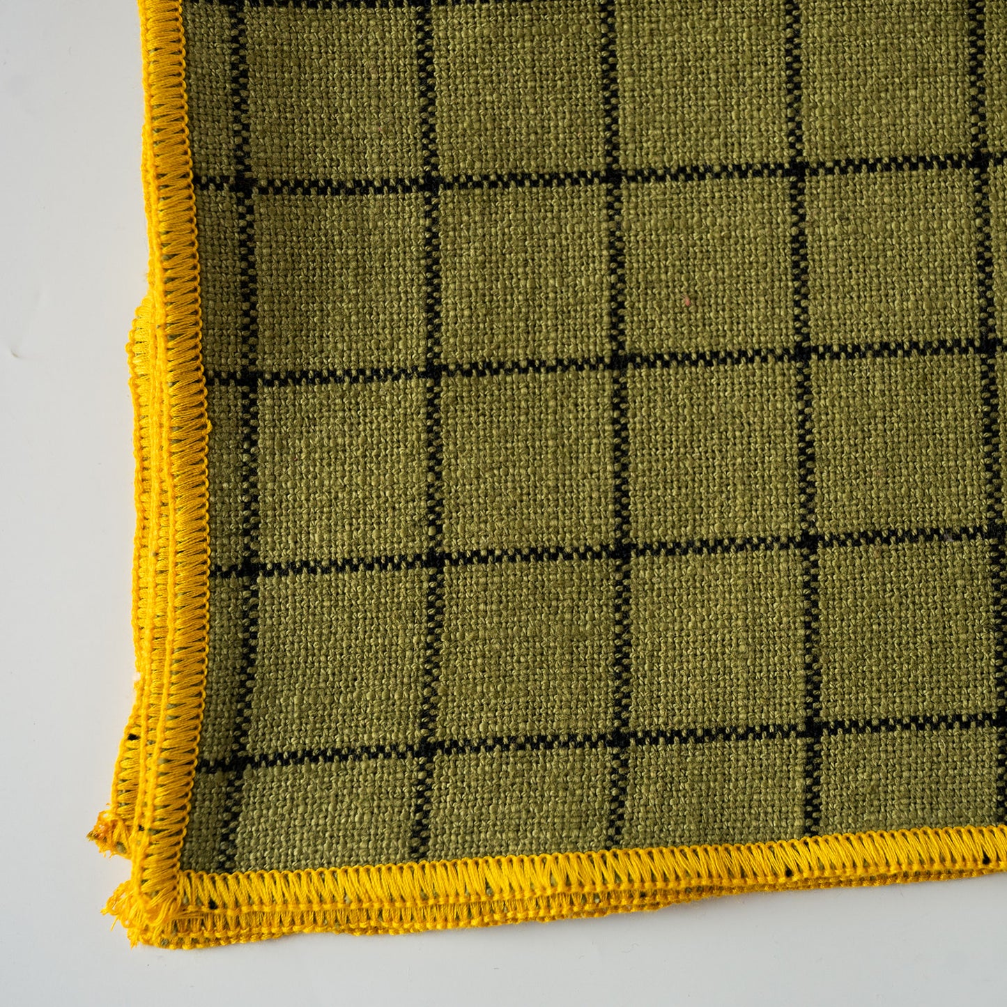 A close-up of a YELLOW woven textile with a black grid pattern and black stitched border, shown on a white background.