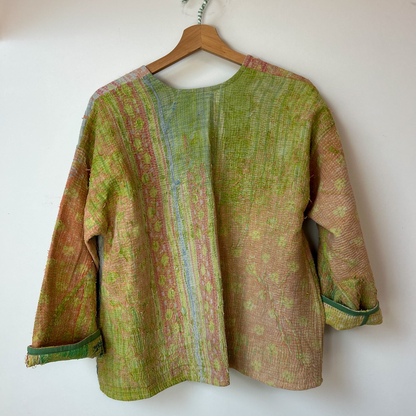 Textured jacket with a mix of green and brown colors on a hanger against a white background. Vintage-kantha-jacket-handmade-unique-41-textured-reverse