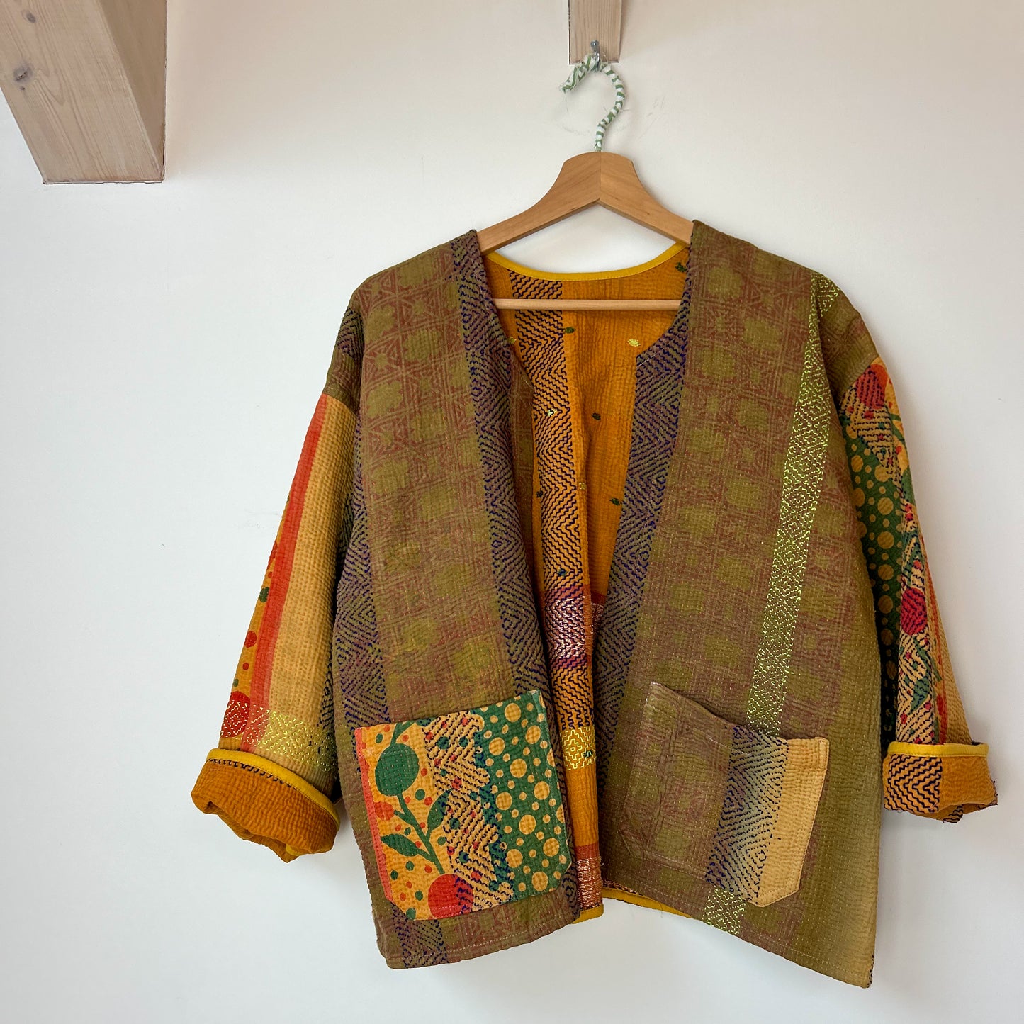 Patchwork jacket with floral patterns on a wooden hanger against a white wall. Vintage-kantha-jacket-handmade-unique-35