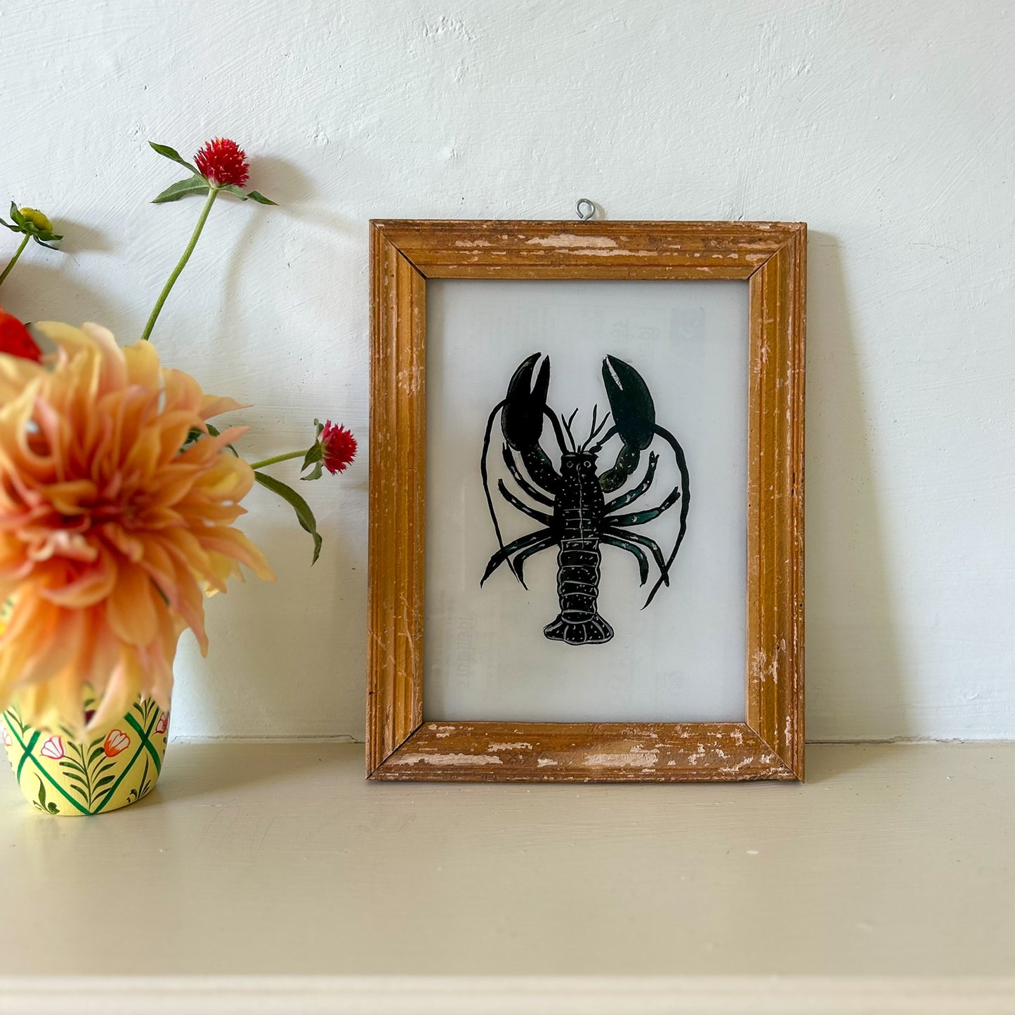 Framed artwork of a black lobster on a white background with a vase of flowers to the left. constance-and-denny-indian-reverse-glass-painting-boxed-packaging-hand-painted-artisan-art-lobster