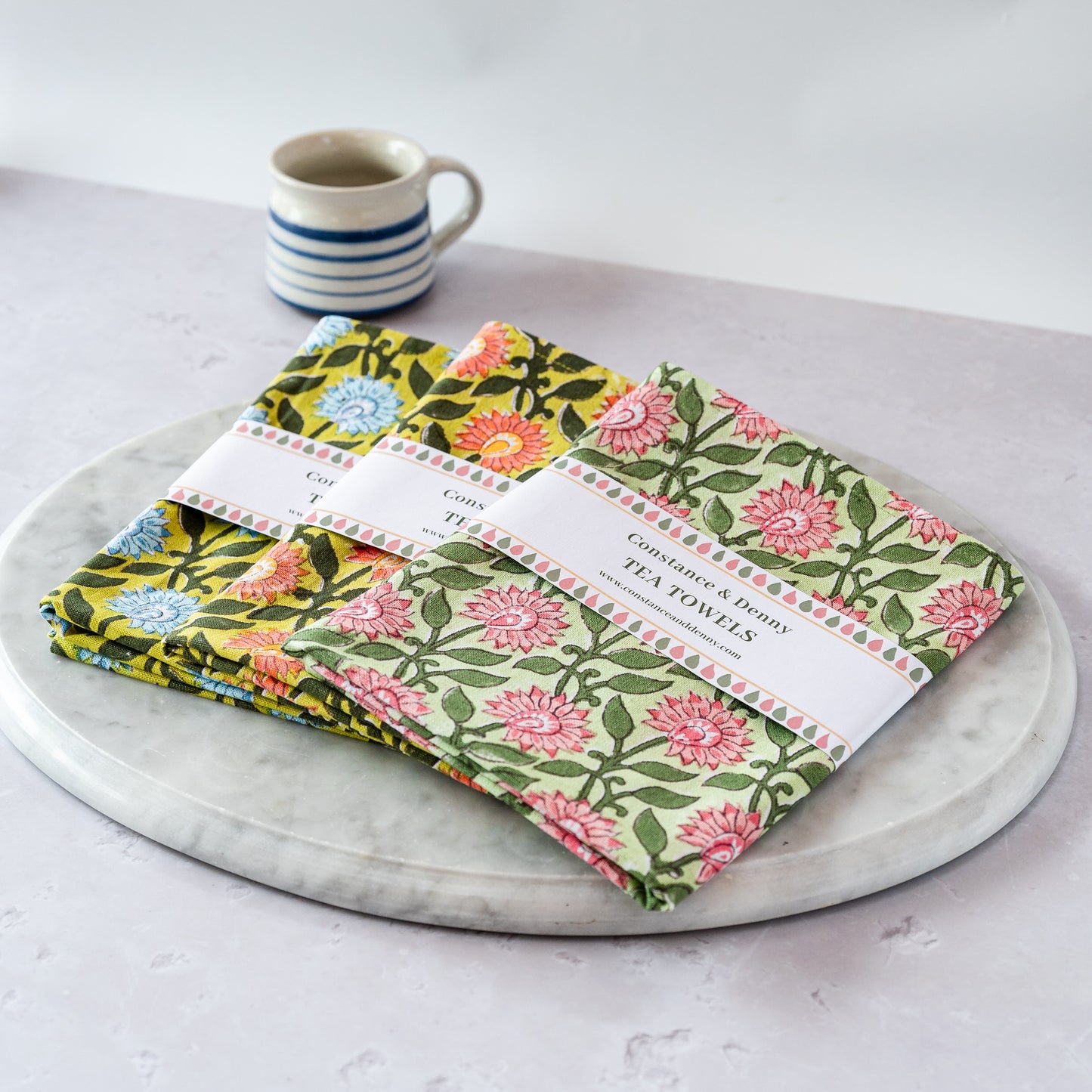 Set of floral tea towels on a marble surface with a mug in the background