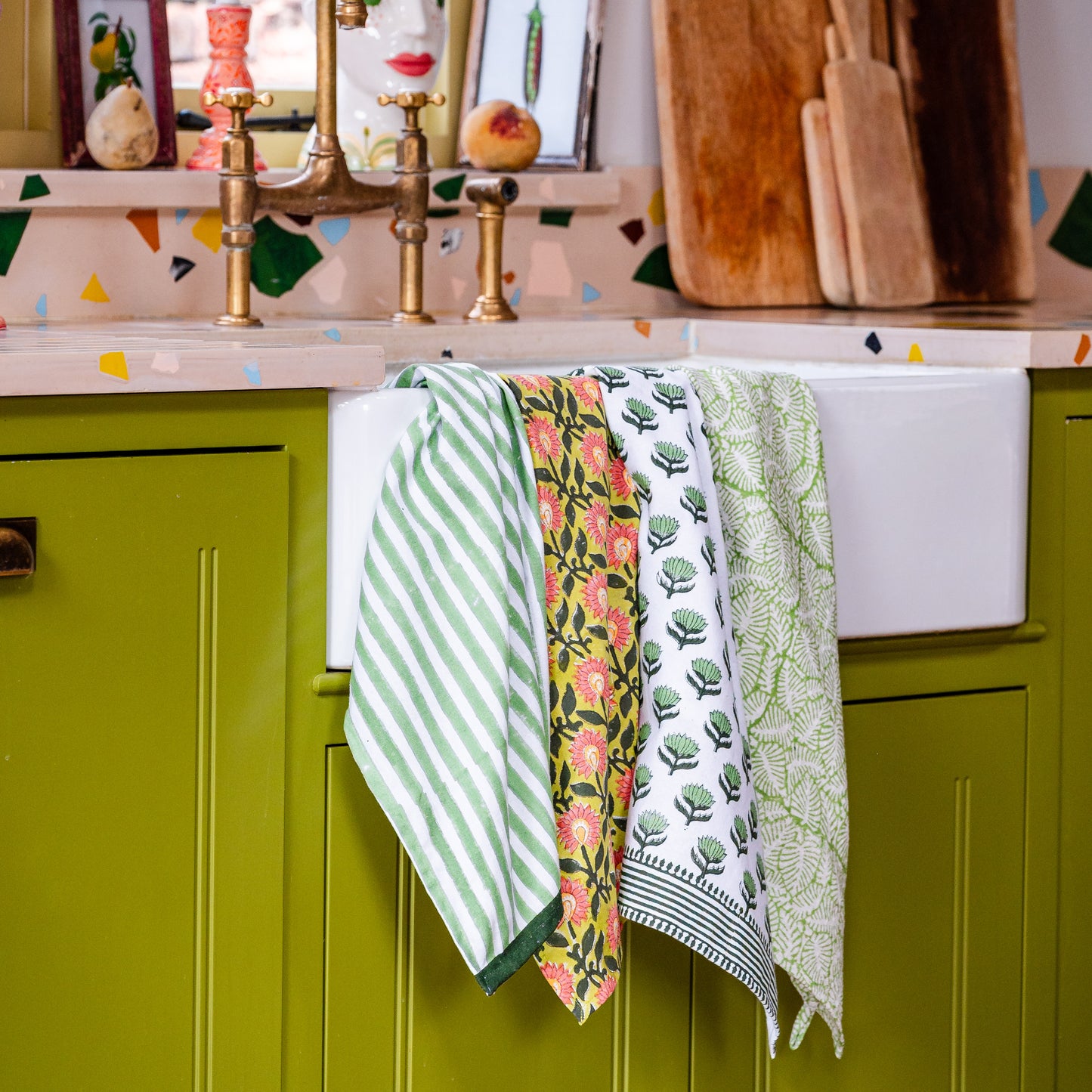 Colorful kitchen scene with green cabinets, floral towels, and a sink.