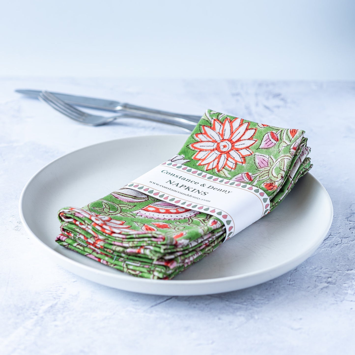 Folded green floral napkins on a white plate with cutlery against a light background. block-printed-set-of-4-napkins-FLORAL-GREEN-NEW-GARDEN