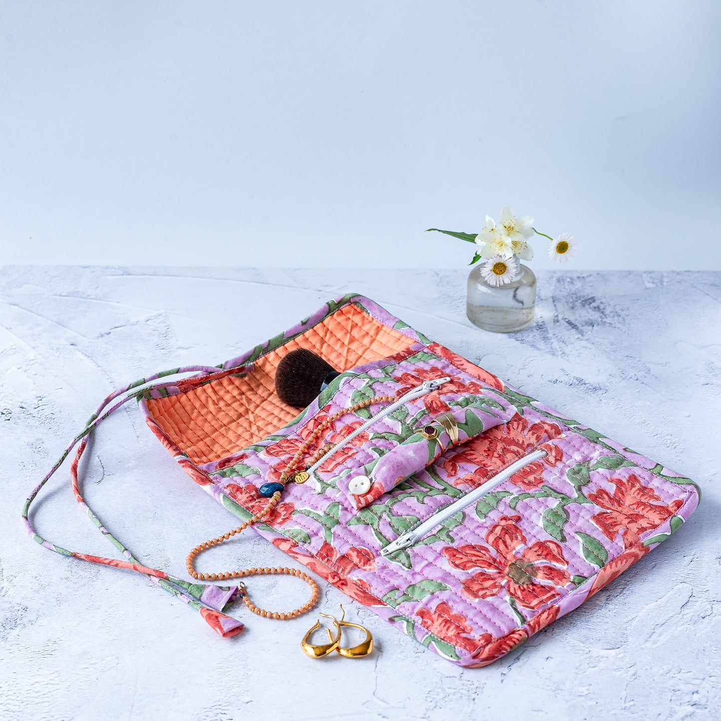 Floral quilted JEWELLERY ROLL with jewelry on a light surface. JEWELLERY-ROLL-BLOCK-PRINTED-QUILTED-CLEMENTINE