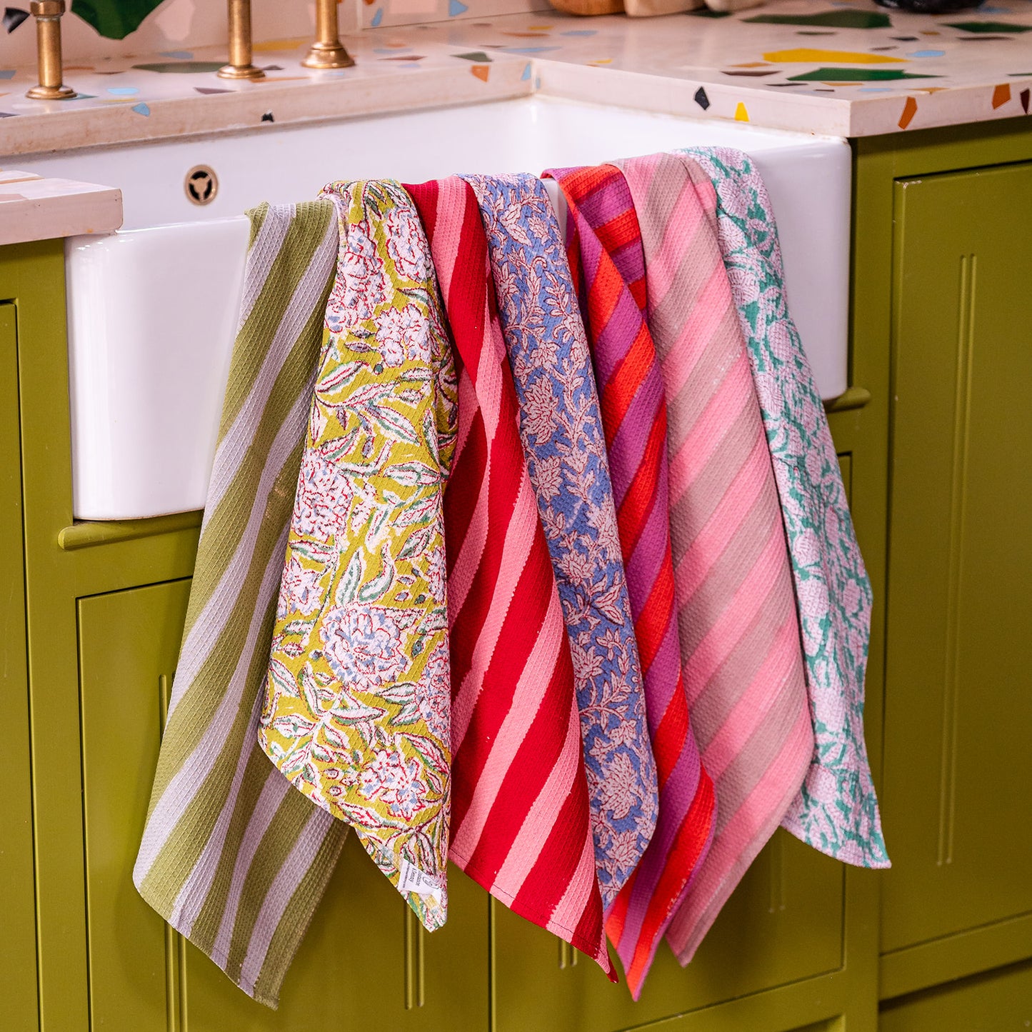 Colorful patterned towels hanging on a kitchen cabinet.