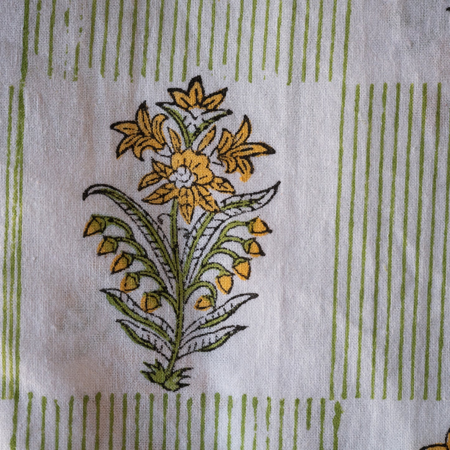 A close-up of a white fabric with a printed floral motif in yellow and green, surrounded by vertical green stripe borders.