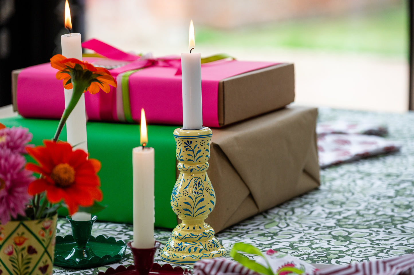 Decorative candles and flowers on a table with wrapped gifts in the background
