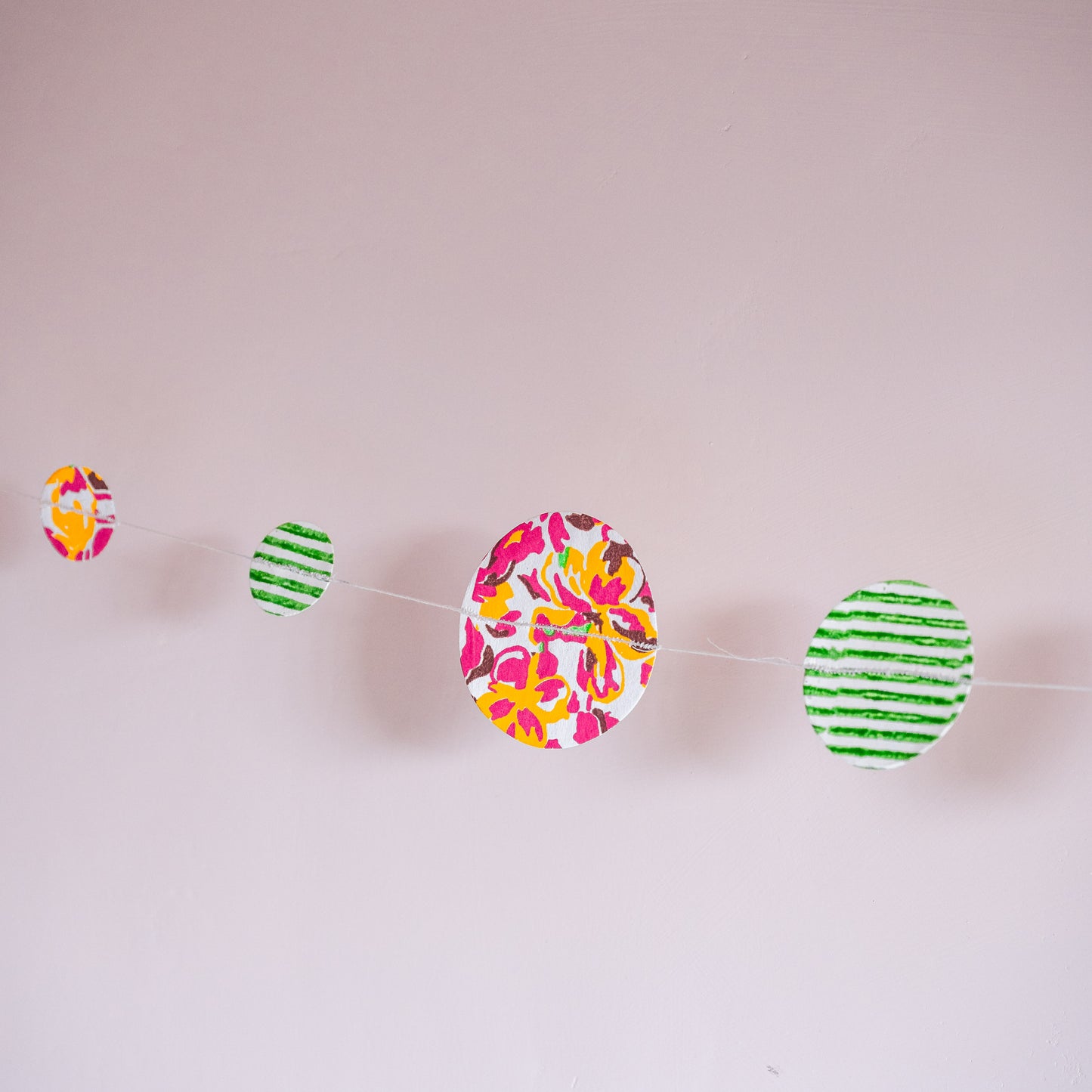 Colorful paper circles on a string against a light pink background