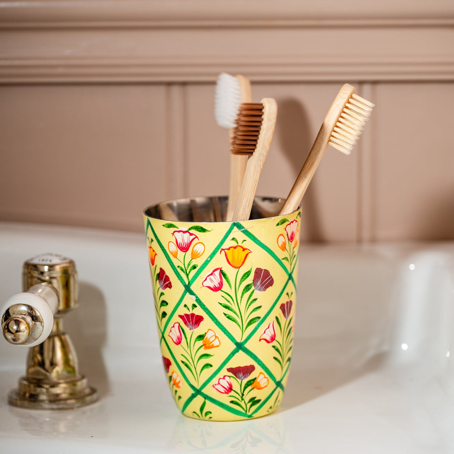 Colorful flowers in patterned vases on a white surface with framed artwork in the background.Vase cream hand painted tooth brush pot