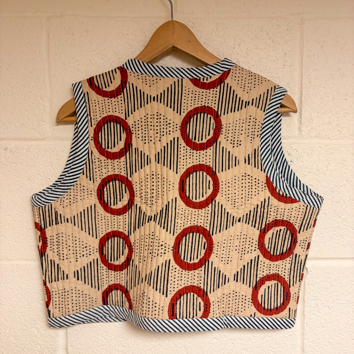 Vest with geometric pattern on a hanger against a white brick wall.