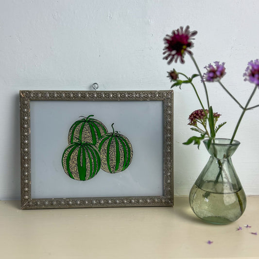 Framed artwork of watermelons next to a vase with flowers on a light surface.  indian-glass-painting-art-reverse-three-watermelons
