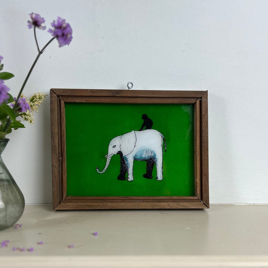 Framed artwork of an elephant on a green background with a vase of flowers beside it. indian-glass-painting-reverse-elephant-with-monkey