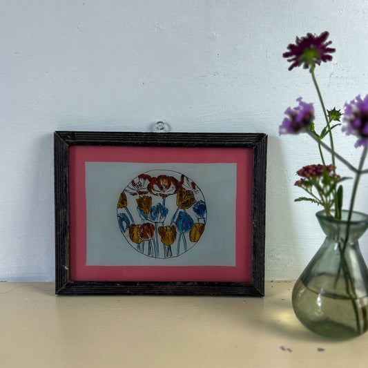 Framed artwork with colorful circular design on a pink background, next to a vase with flowers. indian-glass-painting-painting-circle-tulips
