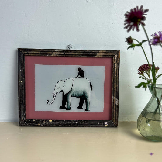 Framed artwork of an elephant and monkey on a pink background, next to a vase with flowers. indian-glass-painting-painting-elephant-monkey-pink-frame
