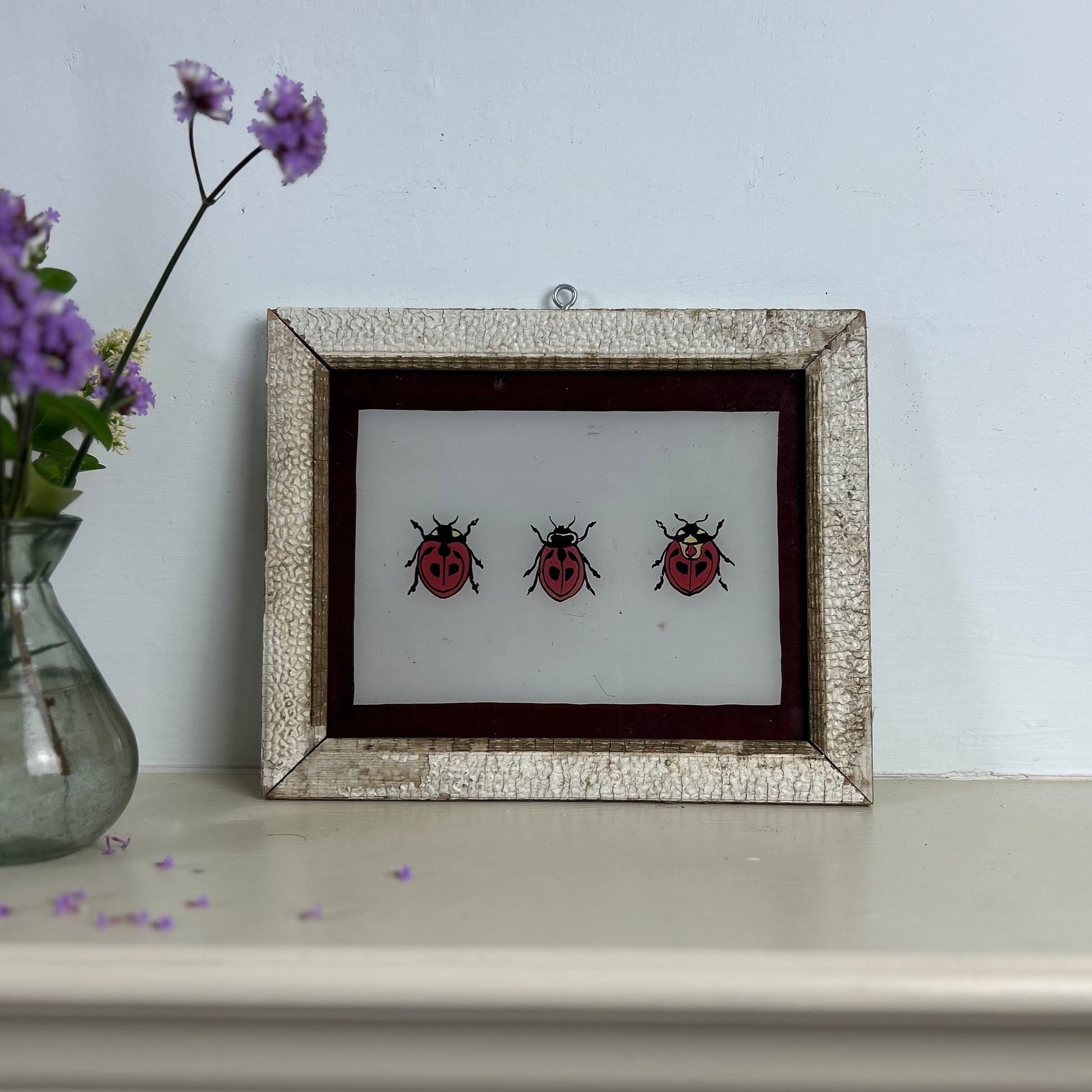 Framed artwork of three ladybugs on a white surface with a light gray wall background. indian-glass-painting-reverse-art-ladybird