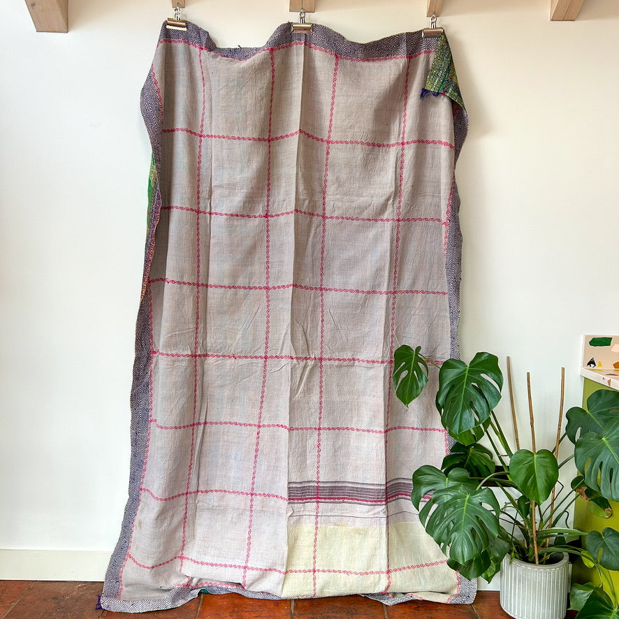 Plaid fabric draped over a wooden frame against a white wall with a plant in the foreground.