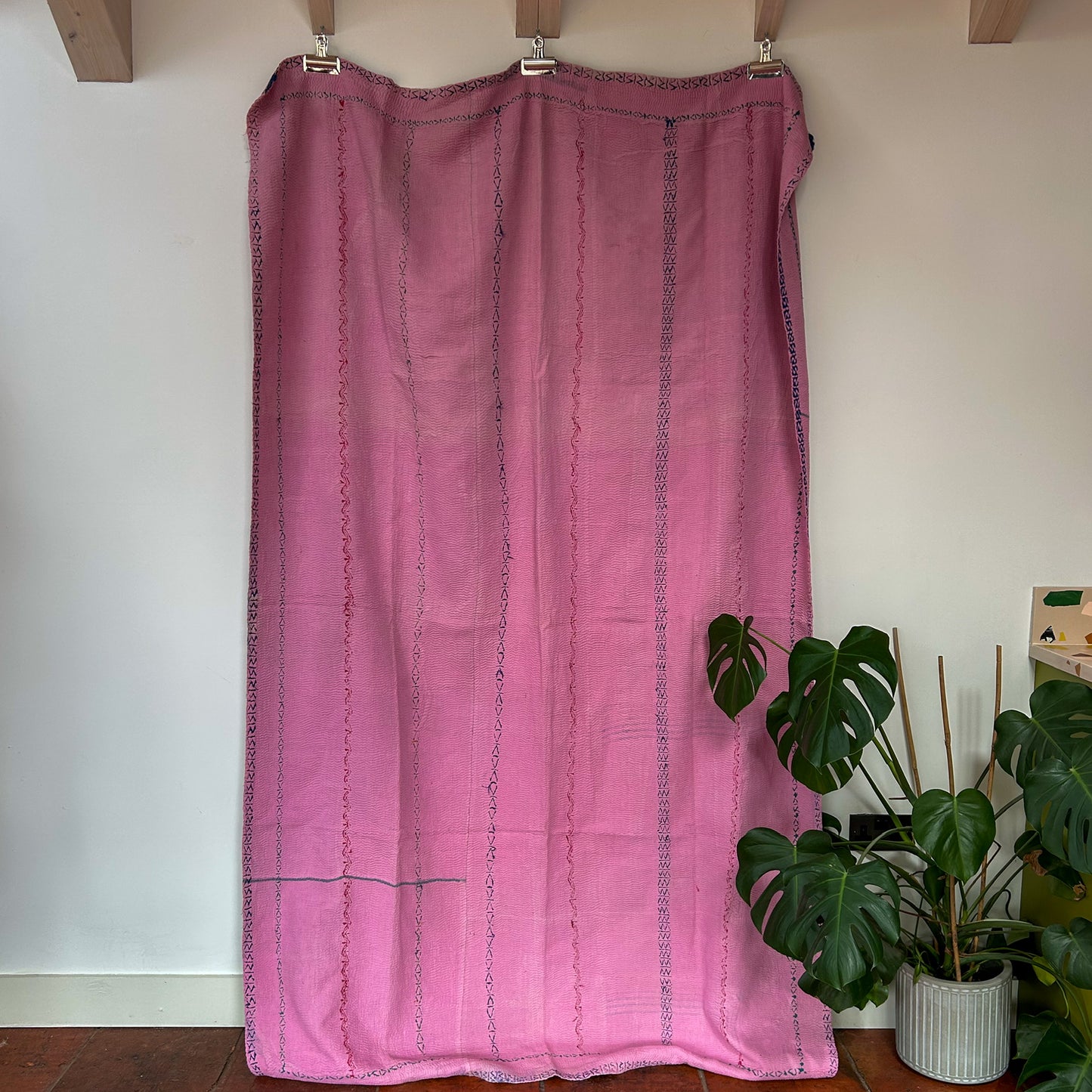 Pink curtain hanging on a wooden rod with a plant in the background. vintage kantha throw 2034