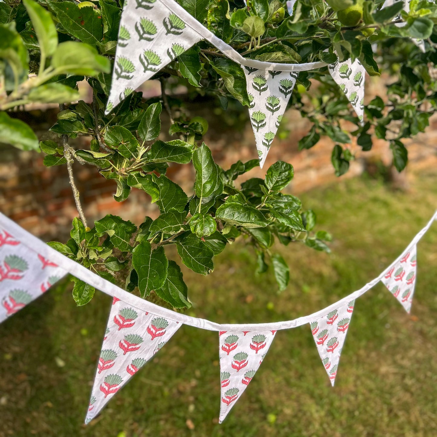 Fabric bunting with floral pattern hanging from a tree. lotus-flower-pink-sage-bunting-block-printed