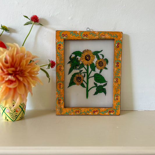 Decorative frame with floral design on a white surface next to flowers. onstance-and-denny-indian-reverse-glass-painting-boxed-packaging-hand-painted-artisan-art-sunflower
