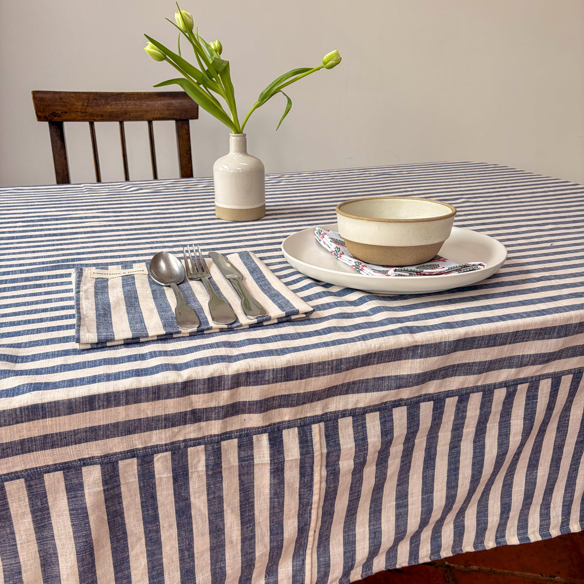 Dining table set with a striped tablecloth, plates, bowls, and cutlery.