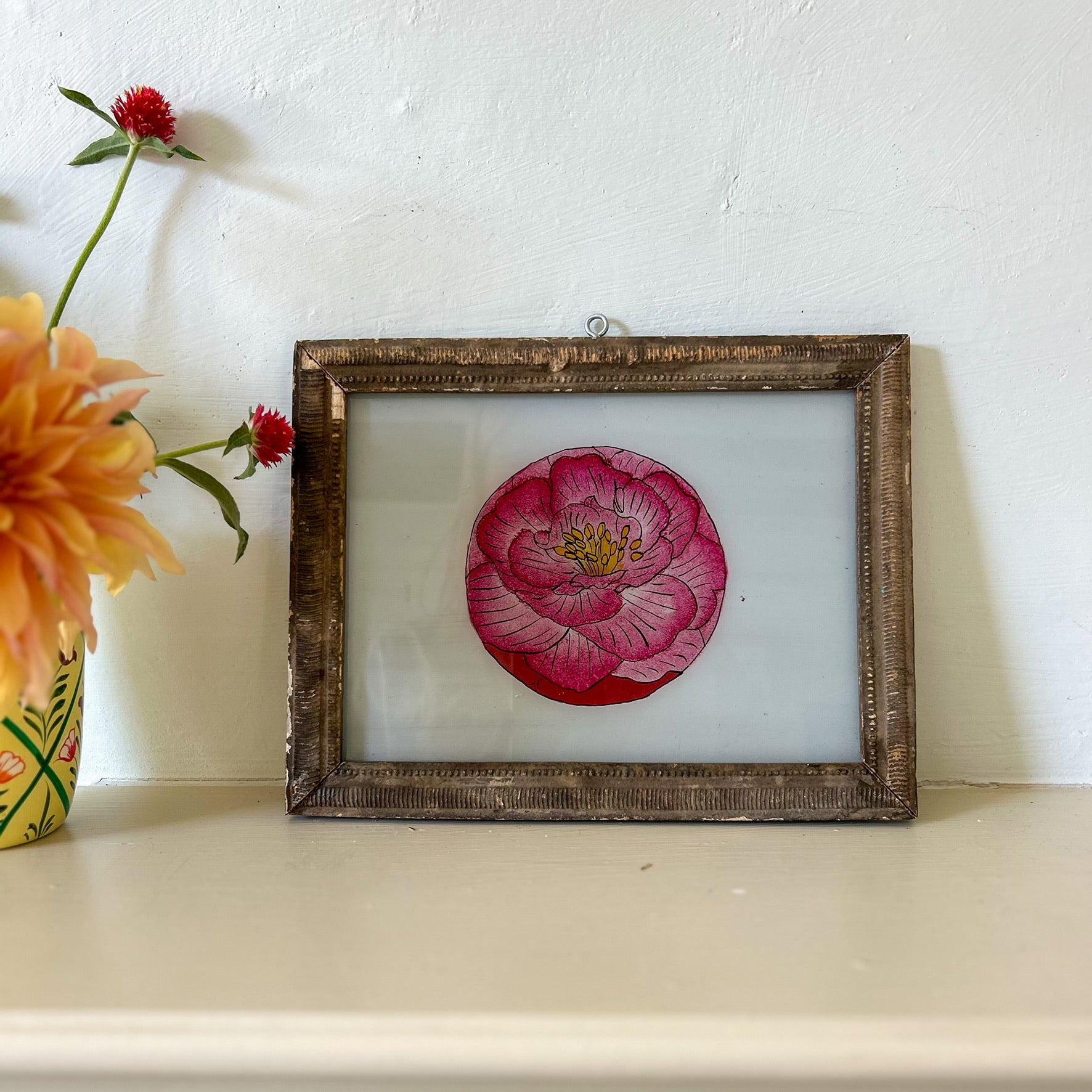 Framed artwork of a pink flower on a white surface with flowers in the background. onstance-and-denny-indian-reverse-glass-painting-boxed-packaging-hand-painted-artisan-art-PINK-FLOWER
