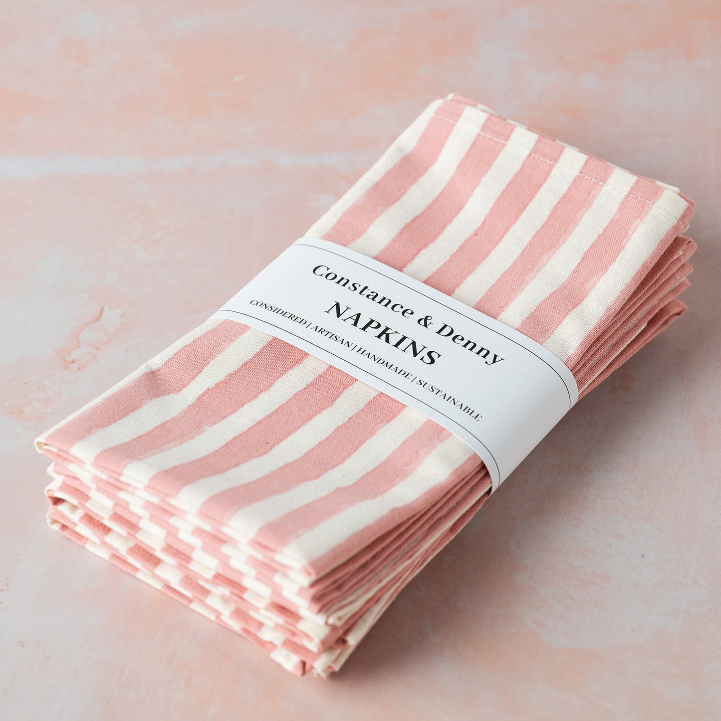 Pack of pink and white striped napkins with 'Constance & Denny' label on a light pink background