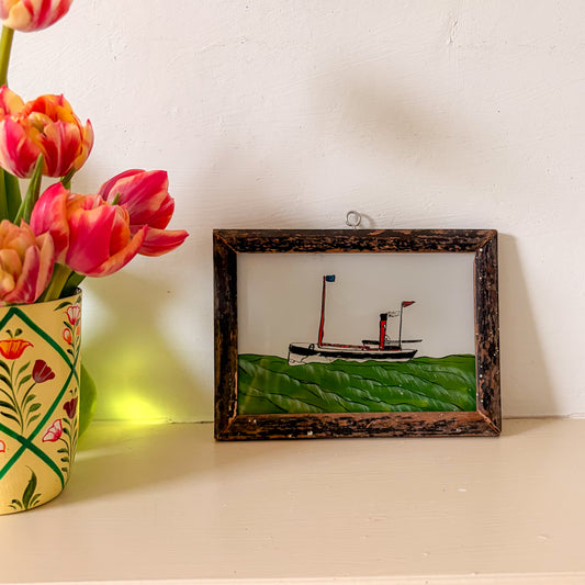 Framed artwork of a ship on a green field next to a vase with pink tulips.