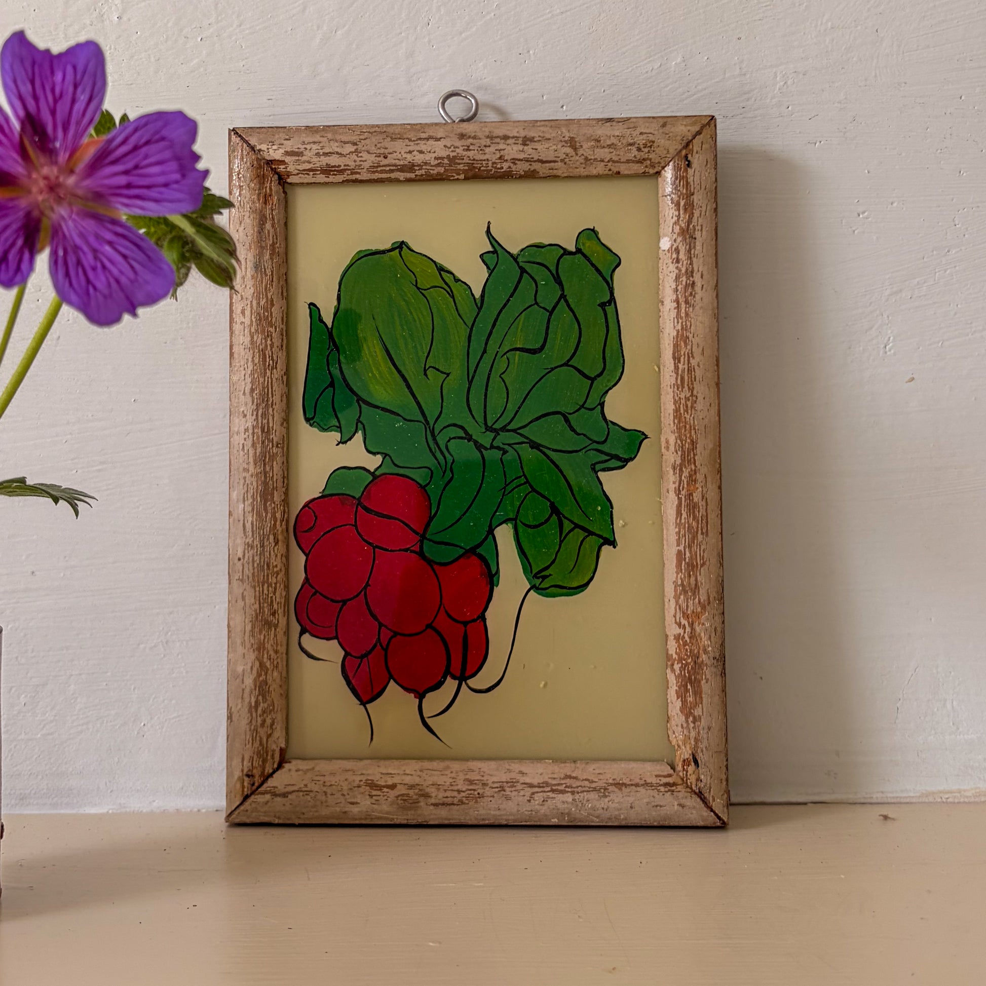 Framed stained glass artwork of raspberries and leaves on a white wall.