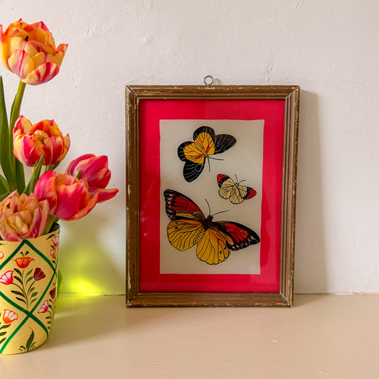 Framed artwork of butterflies on a red background next to a vase of tulips. INDIAN RESERVE PAINTING