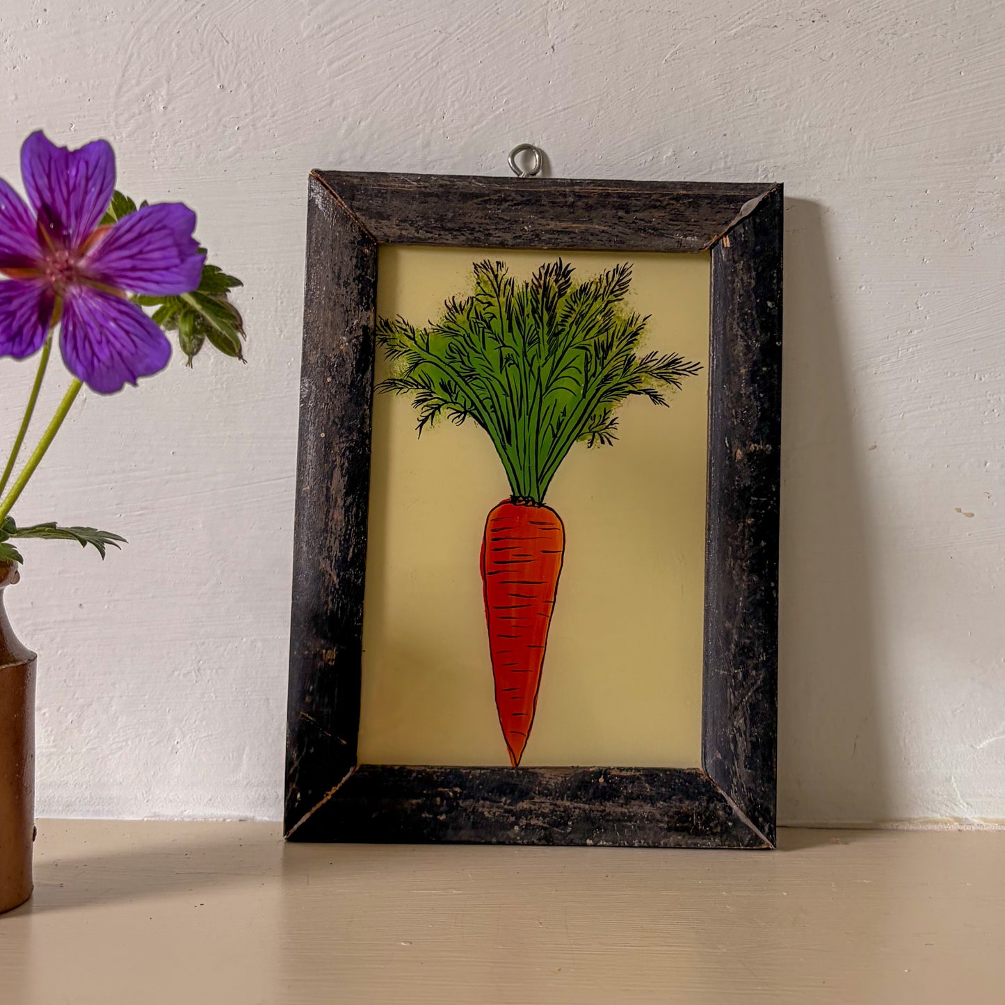 Framed artwork of a carrot on a beige background with a purple flower in the corner.
