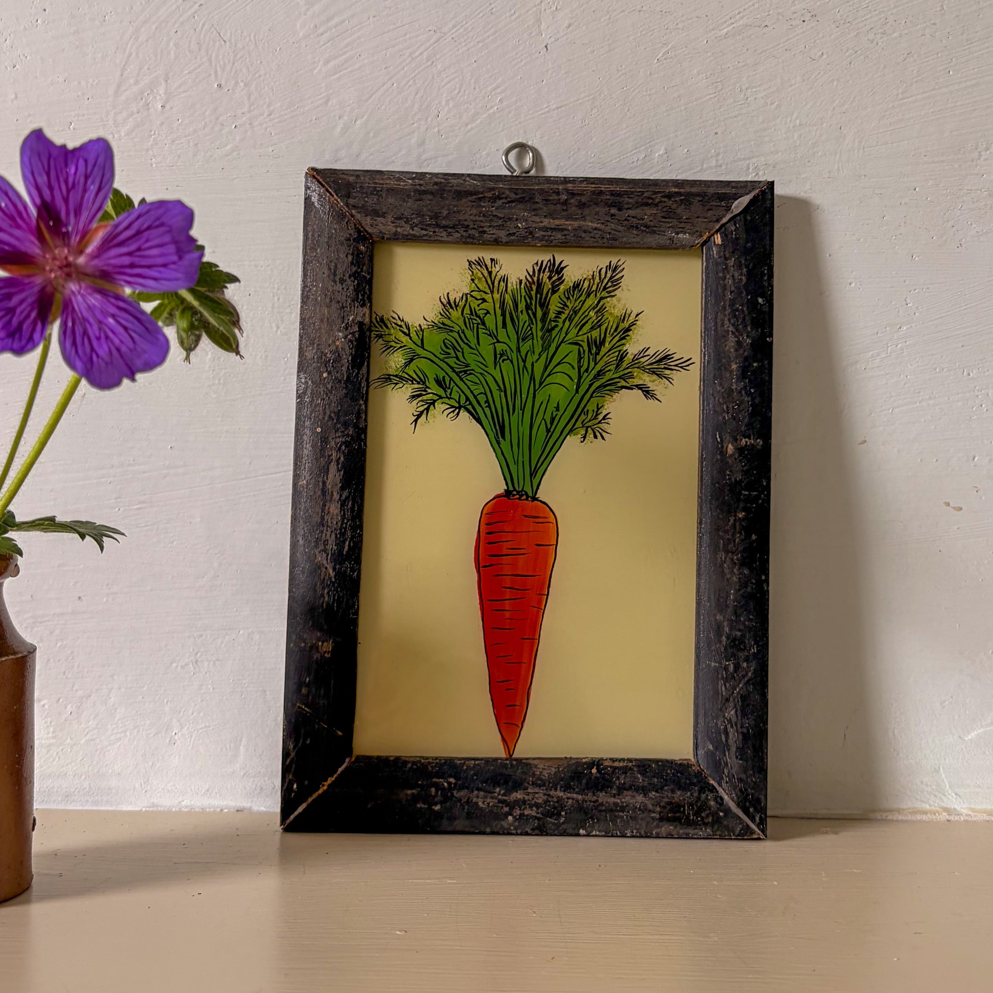 Framed artwork of a carrot on a beige background with a purple flower in the corner.