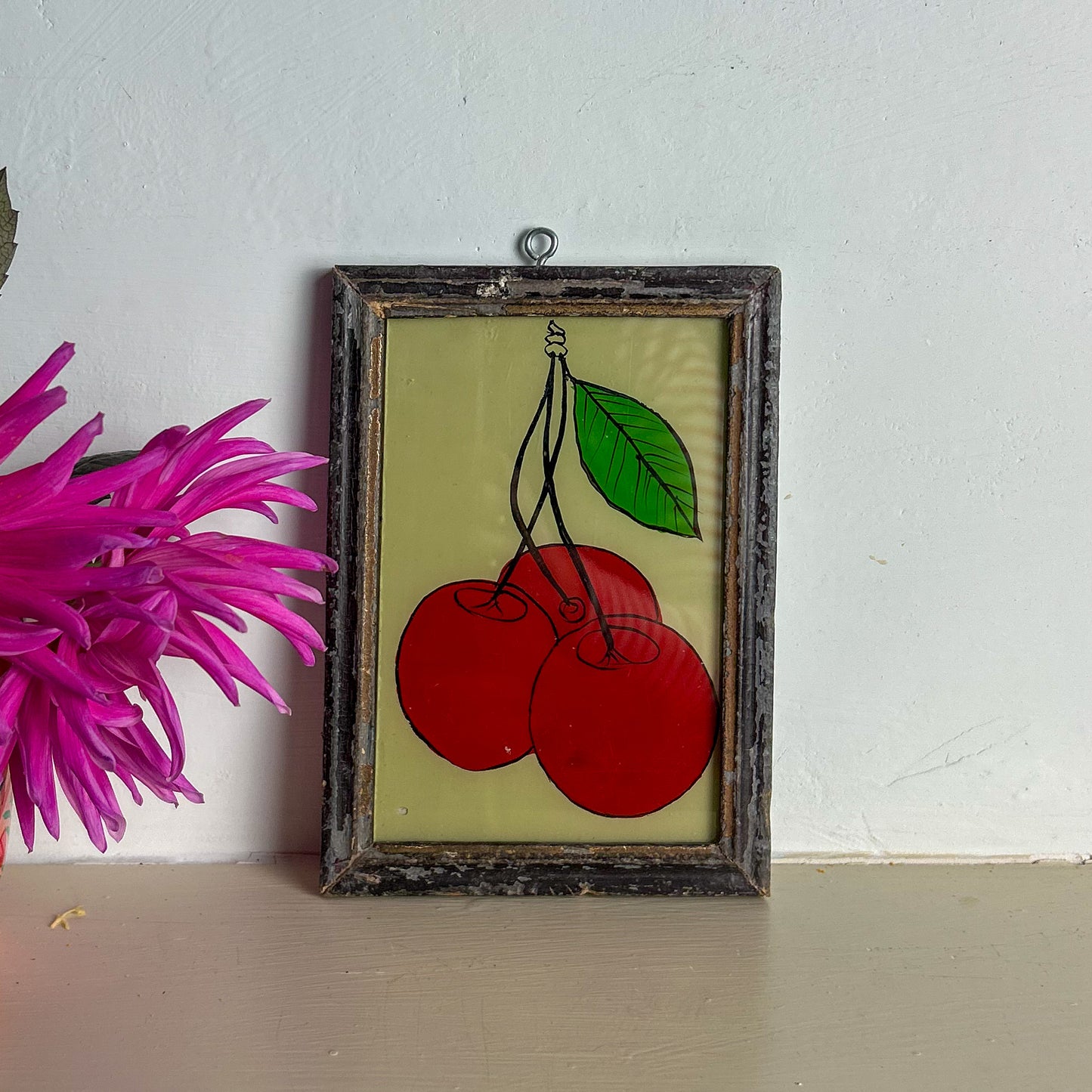 Framed artwork of cherries with a pink flower on a white wall.