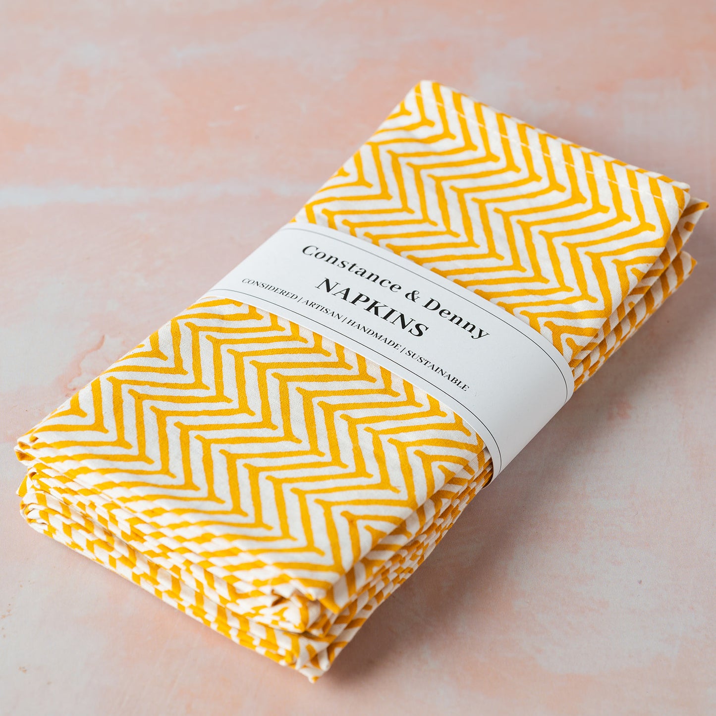 Pack of yellow and white chevron patterned napkins with a visible brand label on a light pink background.