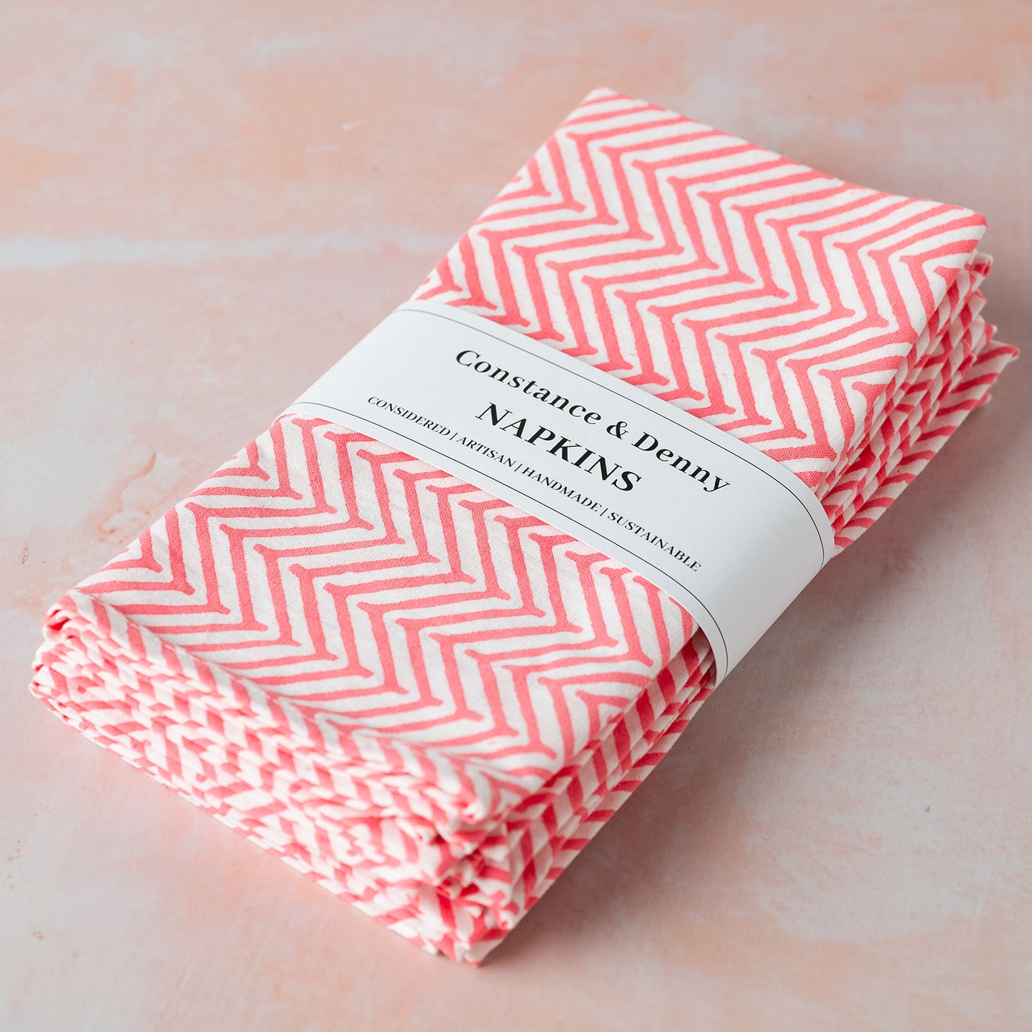 Folded pink and white chevron patterned napkins with a label on a light pink background
