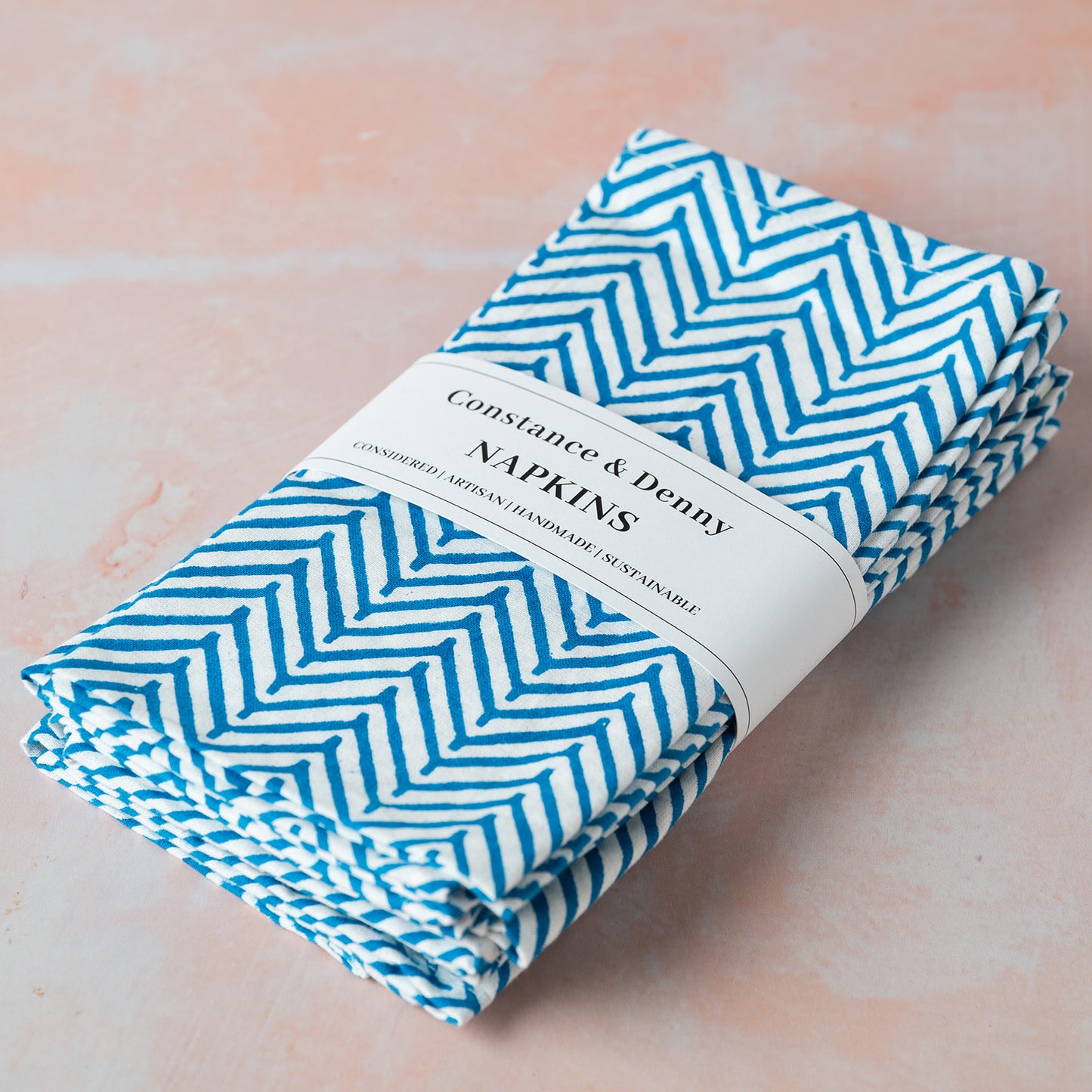Pack of Constance & Denny napkins with blue chevron pattern on a light pink background