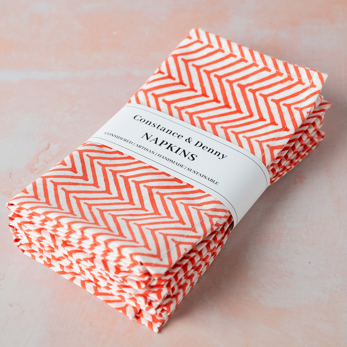 Pack of Constance & Penny napkins with orange chevron pattern on a light pink background