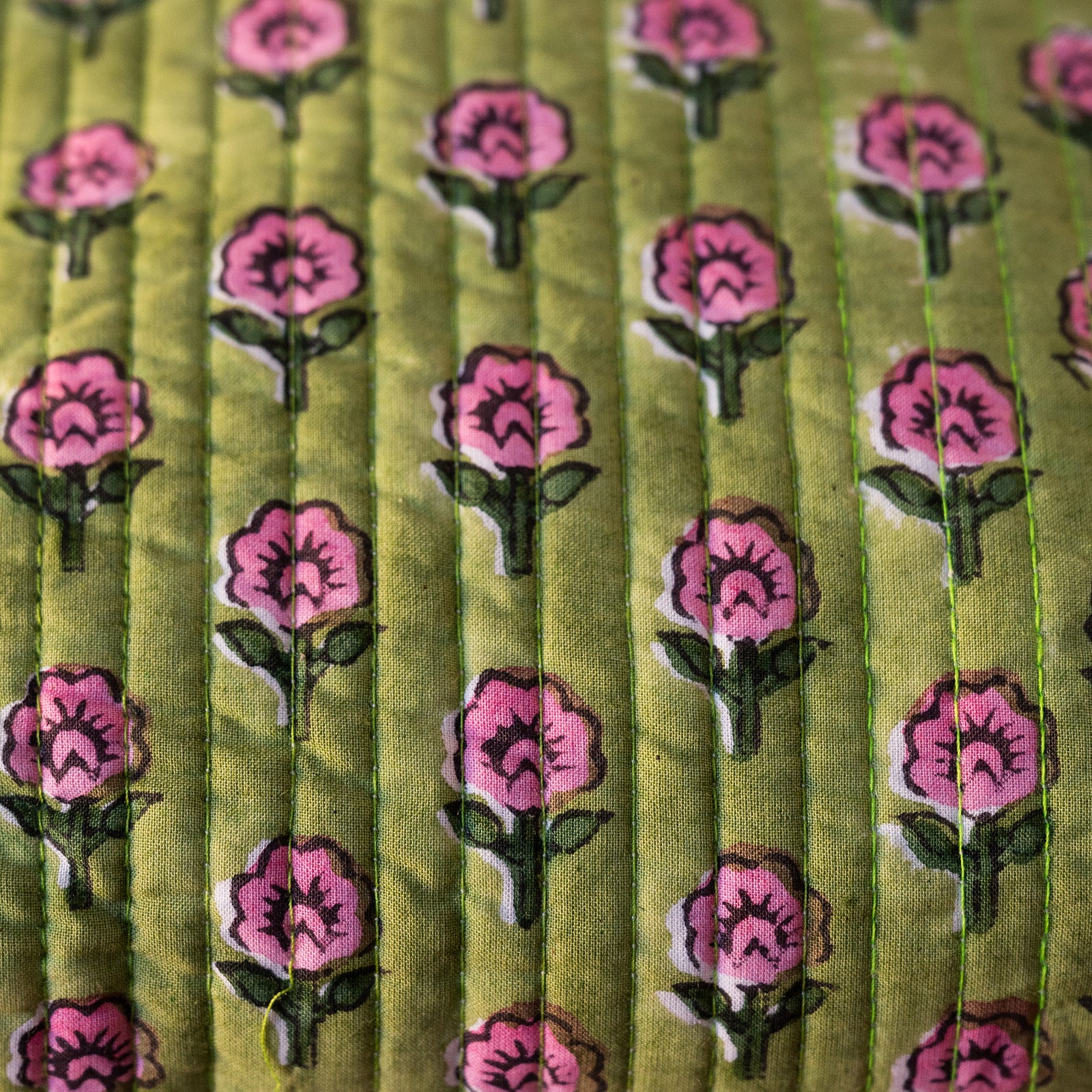 Close-up of a quilted fabric with a repeating floral pattern featuring pink flowers with green stems on an olive green background.