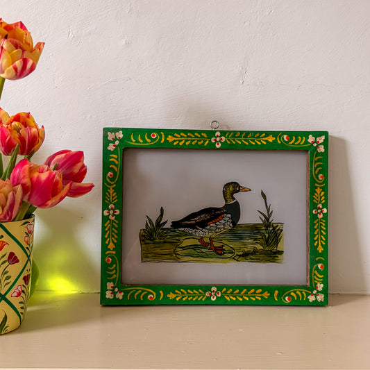 Decorative picture frame with a painted duck design on a white surface next to tulips.