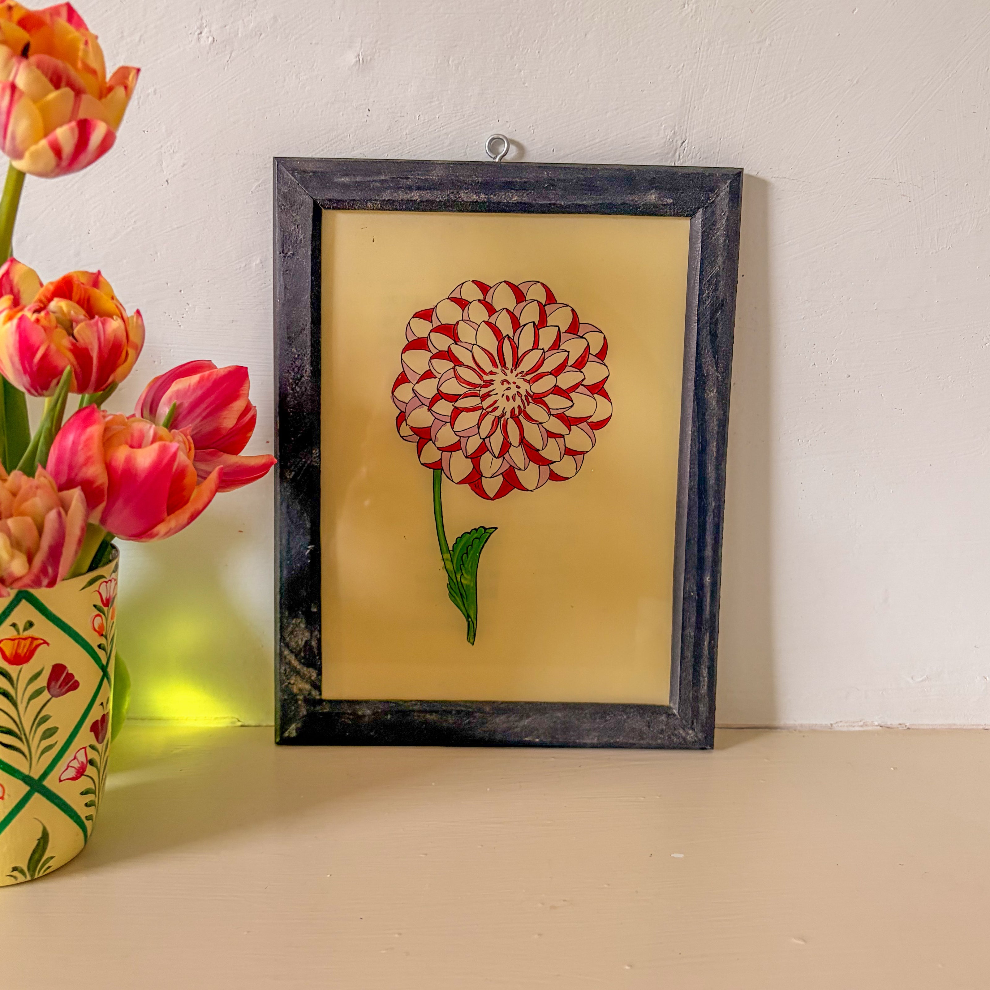 Framed artwork of a red flower on a beige background with tulips beside it. dahlia glass painting