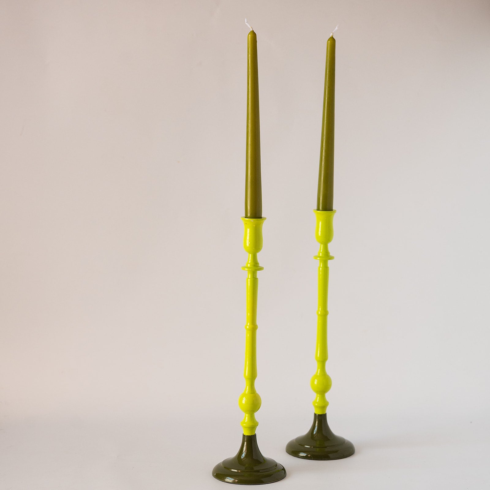 A pair of tall candlesticks with bright yellow-green holders and dark olive-green taper candles, photographed against a plain light background.