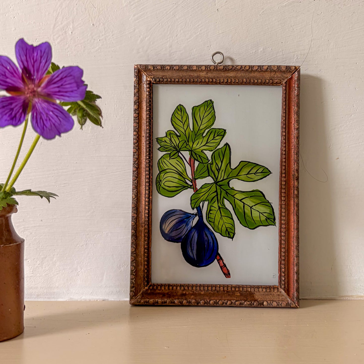 Framed botanical illustration of figs and leaves next to a purple flower in a brown vase.