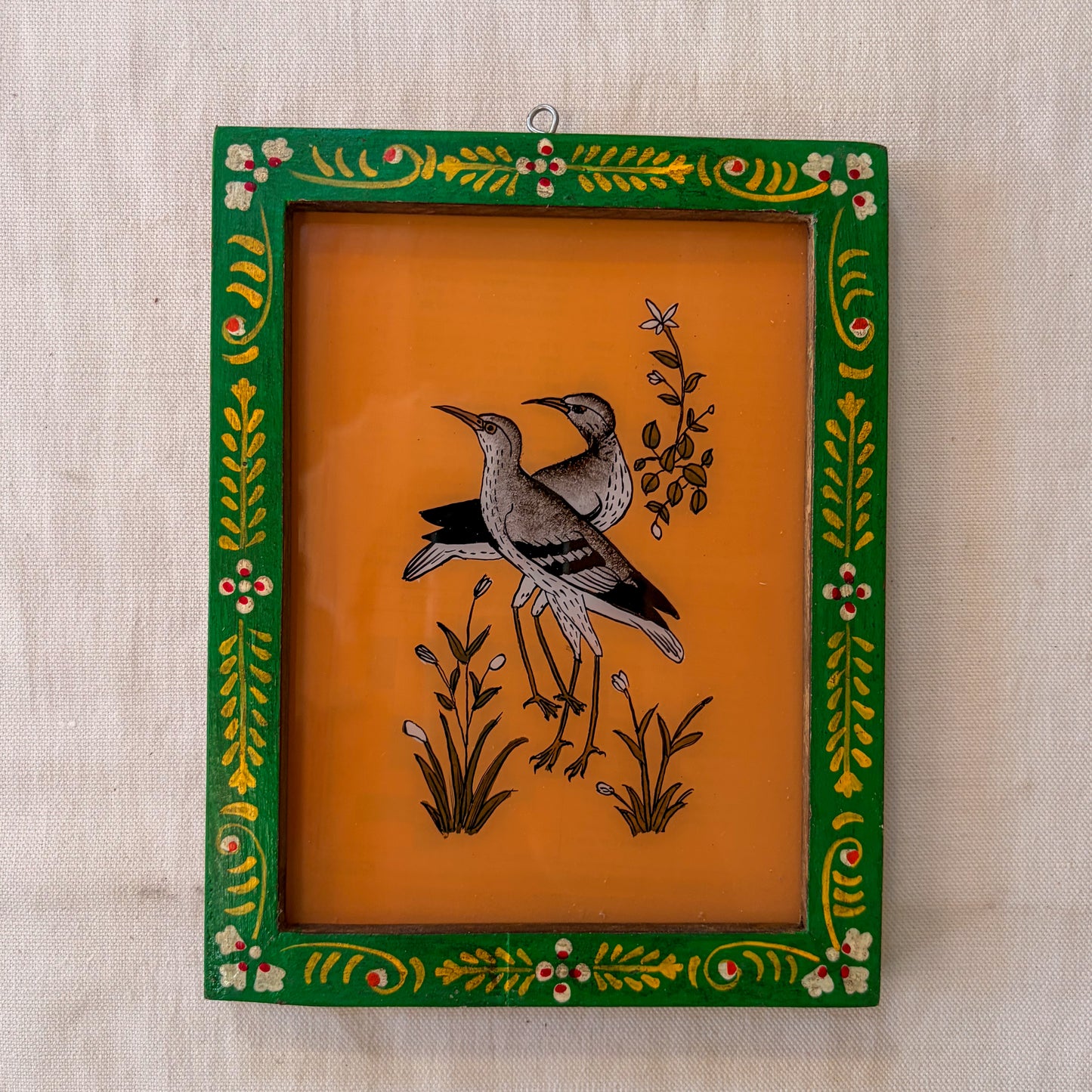 Decorative framed artwork with birds and floral designs on an orange background
