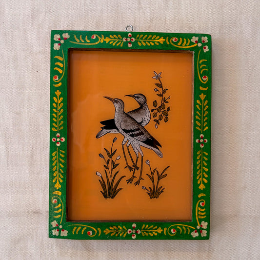 Decorative framed artwork with birds and floral designs on an orange background