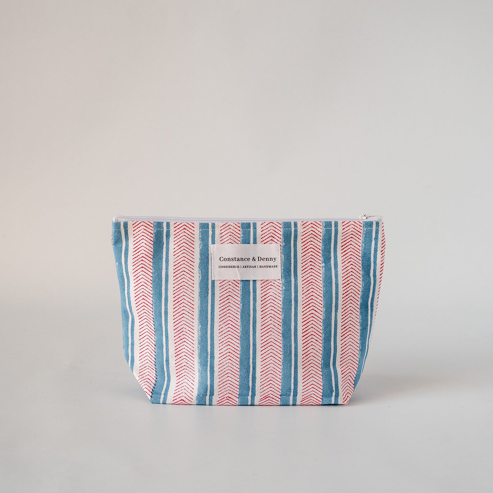 A fabric zippered pouch with vertical stripes in blue, red, and white, featuring a white label that reads 'Constance & Dennis'.