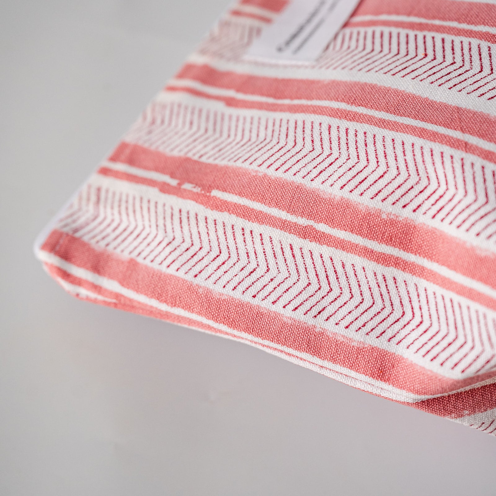 A folded textile item, likely a towel or blanket, featuring a coral pink and white geometric chevron pattern with a small white label visible at the top edge, photographed on a light gray background.